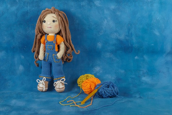 Amigurumi doll handmade on a blue background with the yarns used for its elaboration