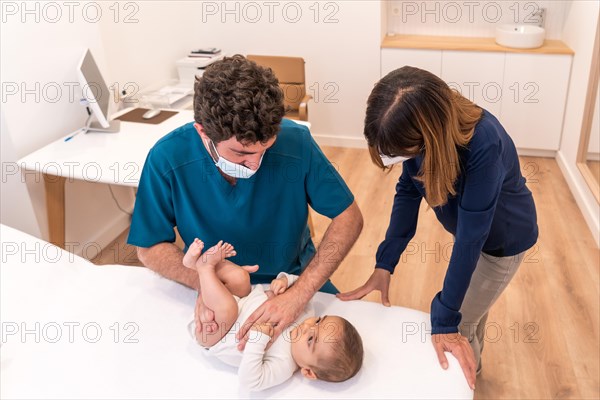 Doctor examining the torso of a baby next to his mother in a clinic