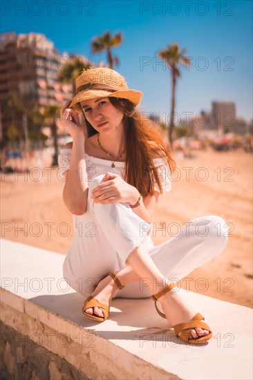 A young red-haired Caucasian girl dressed in white and with a straw hat on the beaches of Calpe