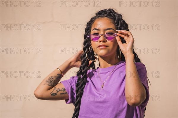 Urban session. Young dark-skinned woman with long braids wearing purple glasses on a plain background