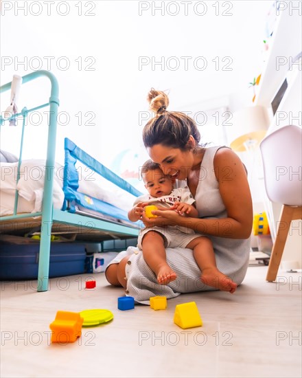 Young Caucasian mother playing with her in the room with toys. Baby less than a year learning the first lessons of her mother. Mother playing with her son and hugging him lovingly