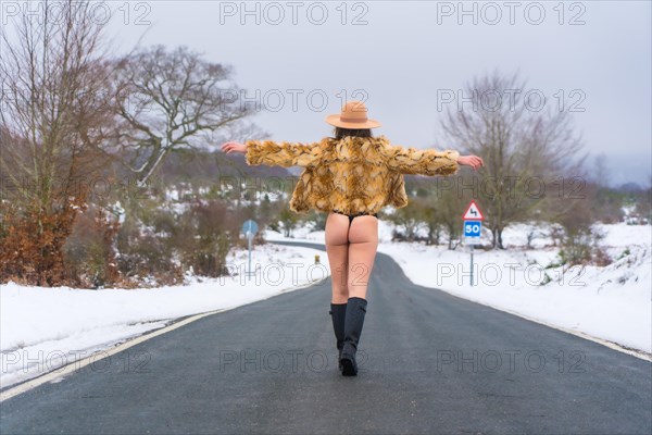 Model girl in underwear and a leopard sweater on a road from behind enjoying the cold