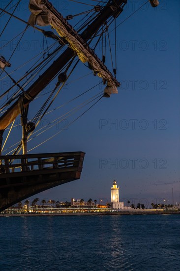 Old ship on the promenade of Muelle Uno in the Malagaport of the city of Malaga and in the background La Farola de Malaga