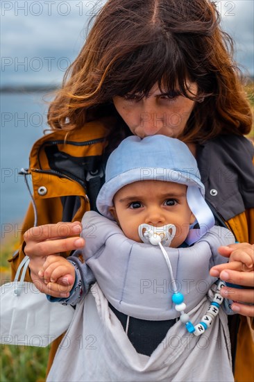 A young mother with her baby at the Phare Du Cap Frehel is a maritime lighthouse in Cotes-dÂ´Armor France . At the tip of Cap Frehel