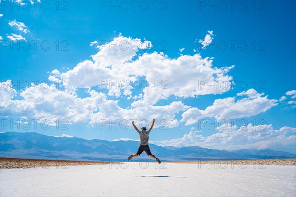 A young man jumping with a blue shirt on the white salt of Badwater Basin