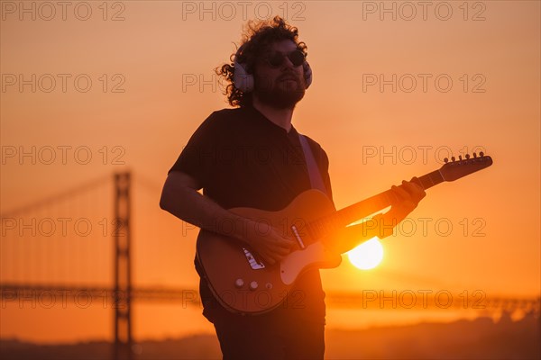 Hipster street musician in black playing electric guitar in street outdoors on sunset