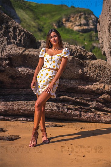 Portrait of a brunette girl in a white dress on the beach enjoying the summer