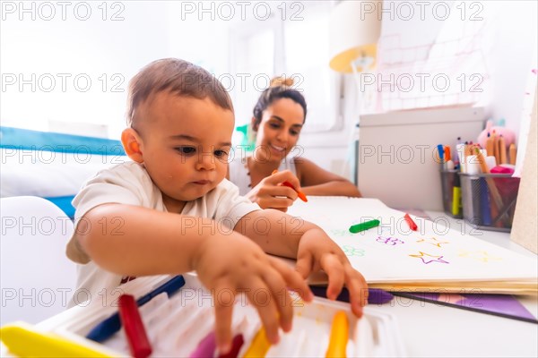 Young Caucasian mother playing with her in the room with toys. Baby less than a year learning the first lessons of her mother. Painting with color paints