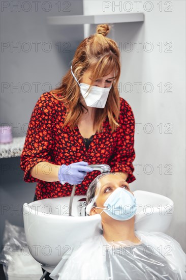 Hairdresser with mask and gloves washing the client's hair with hot tap water and soap. Reopening with security measures for hairdressers in the Covid-19 pandemic
