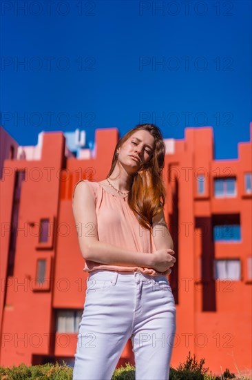 Lifestyle of a young caucasian woman in a salmon colored shirt and white pants in a beautiful colored houses