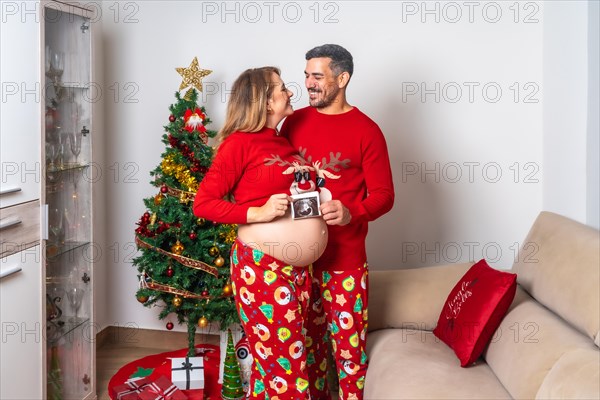 Young couple with red Christmas decorations and clothes having an ultrasound of the new child for the family. Family with pregnant woman