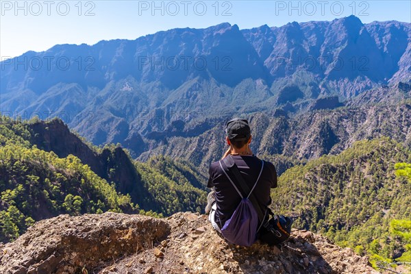 A young man resting after trekking at the top of La Cumbrecita sitting in the natural viewpoint and taking a photo with the mobile