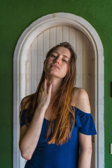 Lifestyle of a young red-haired caucasian girl in a blue dress in a summer perched next to a white door of a green house