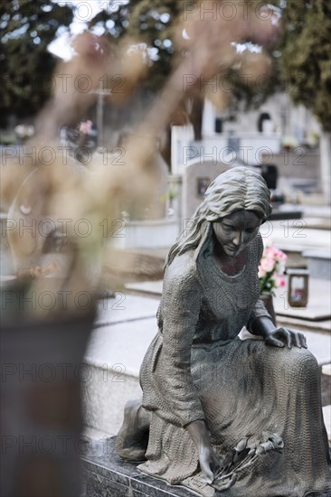 Statue of a mourning woman laying flowers on a grave in a cemetery
