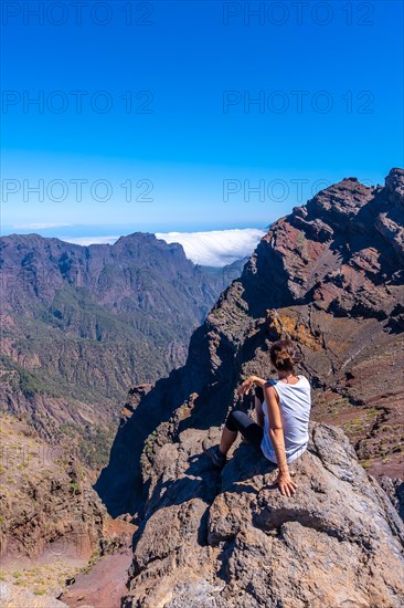 A young woman sits resting and looking at the views of the Roque de los Muchachos national park on top of the Caldera de Taburiente