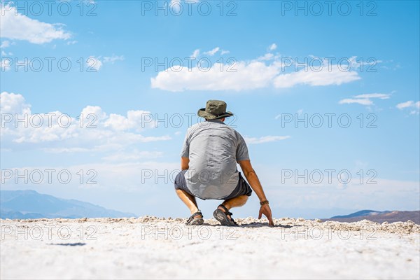 A young man crouched on his back on the white salt flat in Badwater Basin