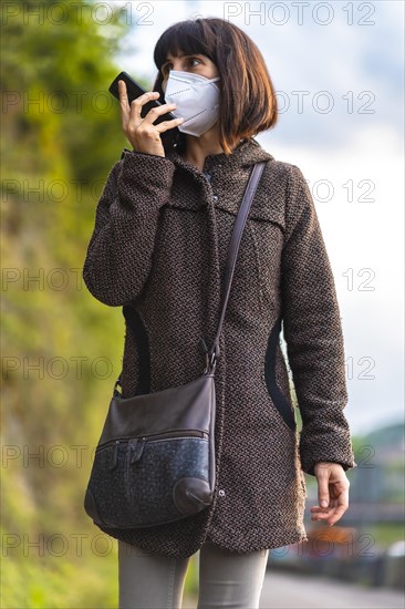 Lifestyle of a young brunette with mask sending an audio message. First walks of the uncontrolled Covid-19 pandemic