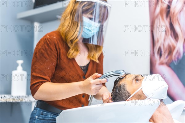 Reopening of hairdressing salons after the Coronavirus pandemic. Hairdresser with face mask and protective screen