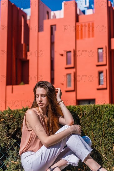Lifestyle of a young Caucasian woman in a salmon-colored shirt and white pants in some colored houses