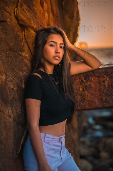 A young pretty brunette Latina with long straight hair in a short black T-shirt and pink pants. Portrait of the woman leaning on a sculpture with scab