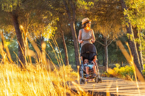 A young woman walking with her son along the wooden walkway in the Donana natural park at sunset. Huelva