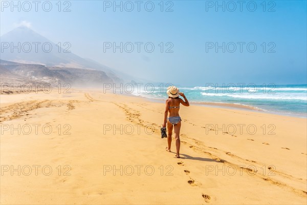 A young woman walking alone on the wild Cofete beach of the Jandia natural park