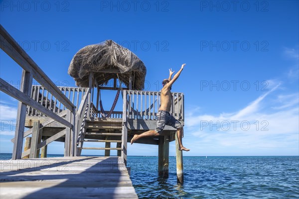 A young man throwing himself into the Caribbean Sea on Roatan Island from a wooden pier. Honduras