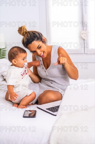Young Caucasian mother with her son in the room on top of the bed. Drink less than a year in a video call with her family. Communication with grandparents in the confinement of the covid-19 pandemic