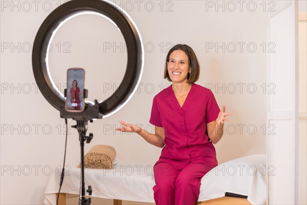 Smiling female doctor recording a tutorial online using a mobile sitting at home