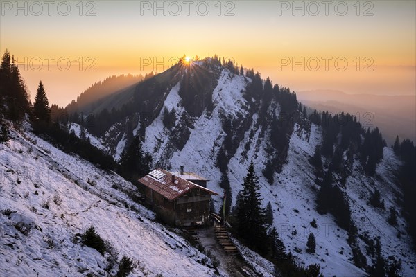 The Staufner Haus on the Hochgrat in autumn at sunset with backlight and sun star. There is snow on the slopes. Oberstaufen