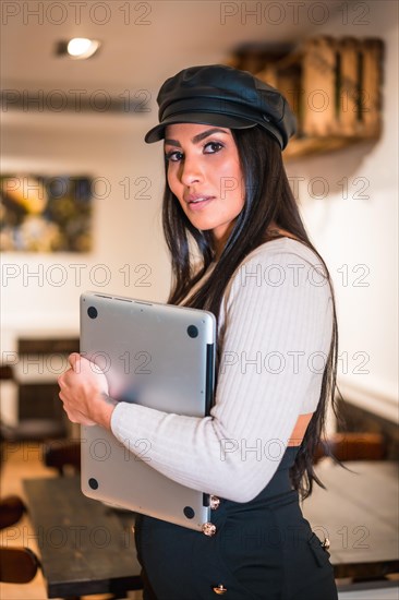 Portrait of a young Latin brunette with a computer teleworking from a cafeteria on vacation