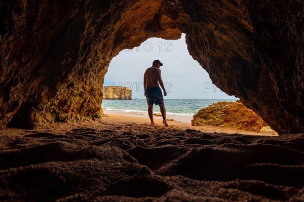 A man in the natural cave in the Algarve in summer on the beach at Praia da Coelha