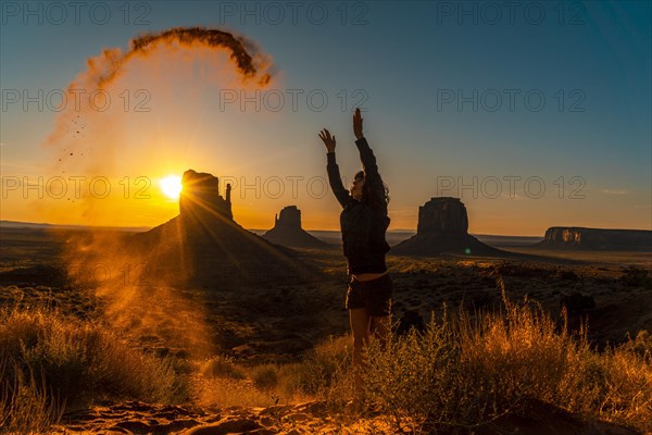 A brunette lifestyle girl at the dawn of Monument Valley playing with the sand