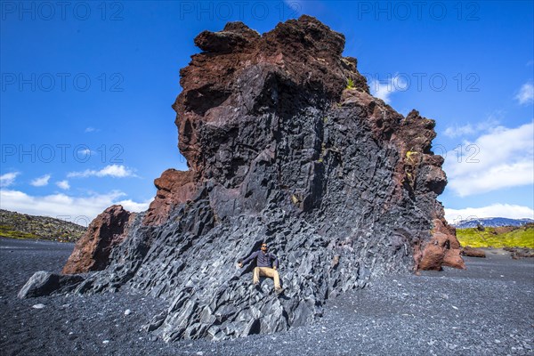 A young man on top of some rocks sitting on the black beach of the Snaefellsnes coast. Iceland