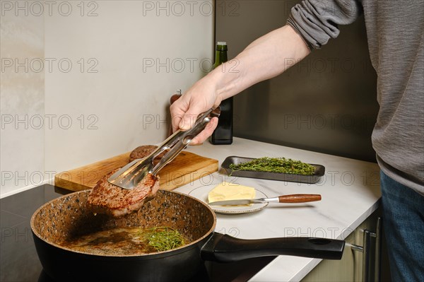 Close up view of taking out frying pan fried beefsteak with kitchen tongs