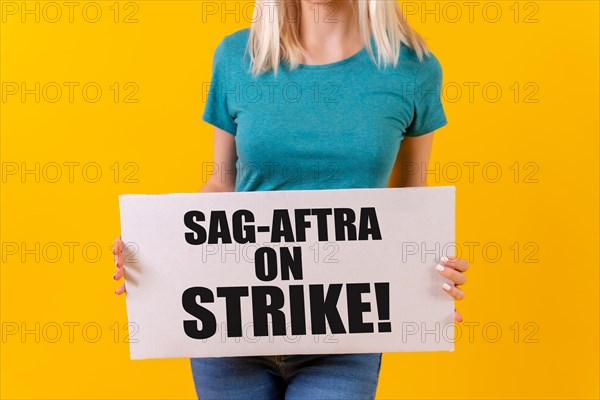 A female actress holding a sign with the hollywood actors and writers strike slogan on a yellow background