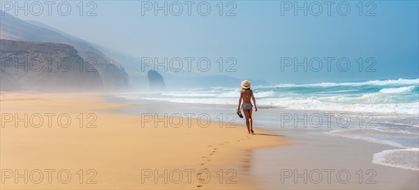 Panoramic of a young tourist with a hat walking alone on the Cofete beach of the Jandia natural park