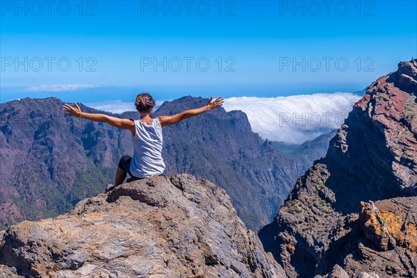 A young woman sits resting and looking at the views of the Roque de los Muchachos national park on top of the Caldera de Taburiente