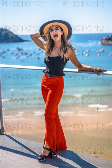 Blonde woman in a luxury hotel on a terrace wearing a hat with sunglasses and the sea in the background