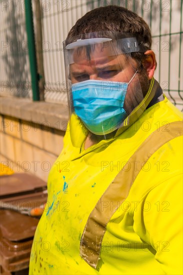 Worker in a recycling factory or clean point and garbage with a face mask and plastic protective screen