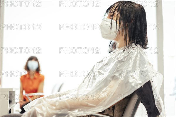 One client with a mask waiting for the cut and another client in the background. Reopening with security measures of Hairdressers in the Covid-19 pandemic