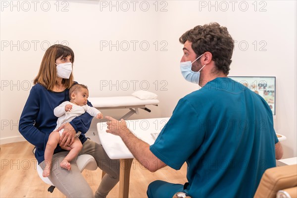 Rear view of a young doctor talking to mother with a baby in the clinic