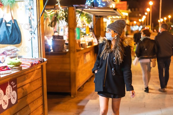 Christmas lifestyle in a new normal. Young girl with face mask visiting the Christmas market in the coronavirus pandemic