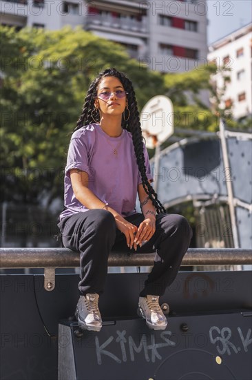 Mischievous gaze of young dark-skinned woman in purple shirt holding long braids