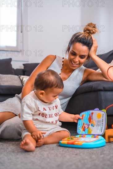 Young Caucasian mother with her son sitting on the floor next to the black sofa. Teleworking and caring for your child
