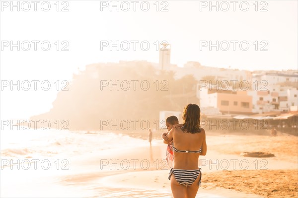 A young mother with her six-month-old baby at sunset on a beach