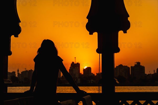 A young woman looking at the orange sunset on the Nile River from a boat leaning on the railing