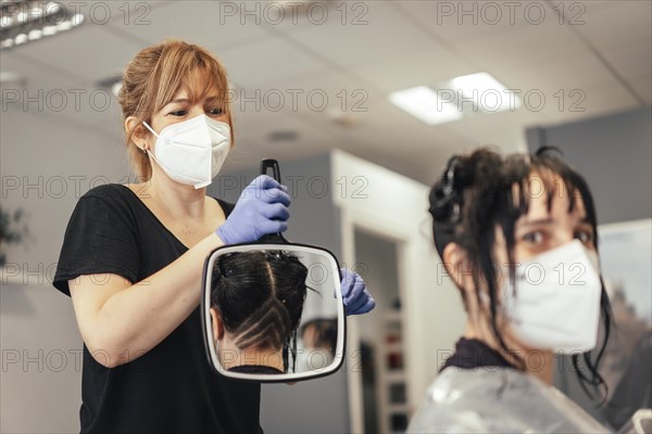 Hairdresser with mask teaching cut in the mirror. Reopening with security measures of Hairdressers in the Covid-19 pandemic