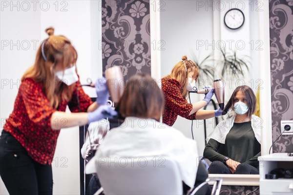 Hairdresser with mask and gloves smoothing hair of client dryer. Reopening with security measures for hairdressers in the Covid-19 pandemic