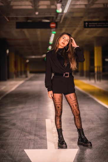 Young Caucasian model perched on the asphalt of an empty underground car park. Night urban session in the city